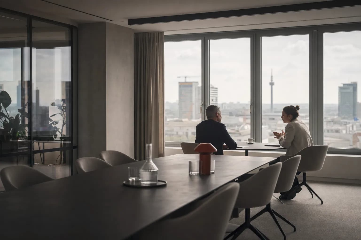 Ruhiger Besprechungsraum mit langem Tisch und zwei Personen im Gespräch.